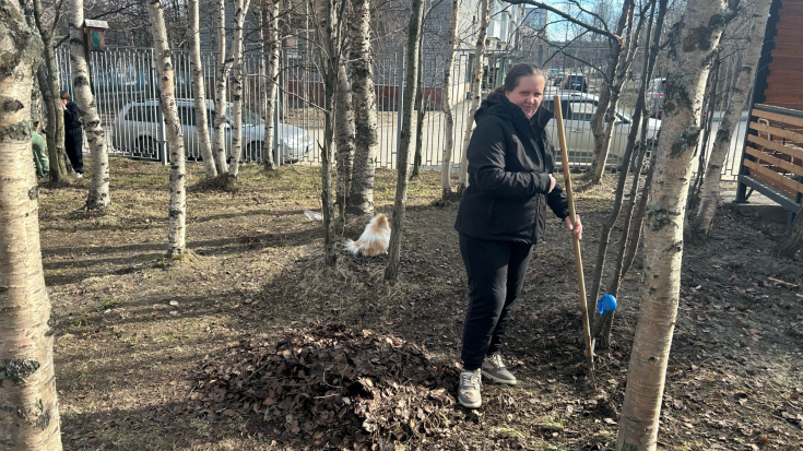 Женщина осуществляет сбор сухой листвы с поверхности земли при помощи граблей